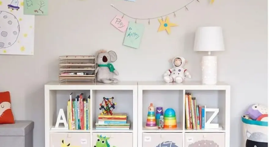 Soluzione creativa per come sistemare i giochi in salotto: scaffali bianchi con contenitori decorati e libri ordinati.