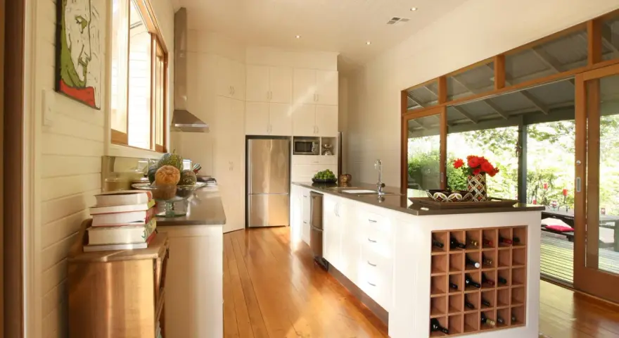Cucina moderna con isola centrale dotata di una cantina a vista per il vino. Ampie vetrate si aprono su un patio esterno.