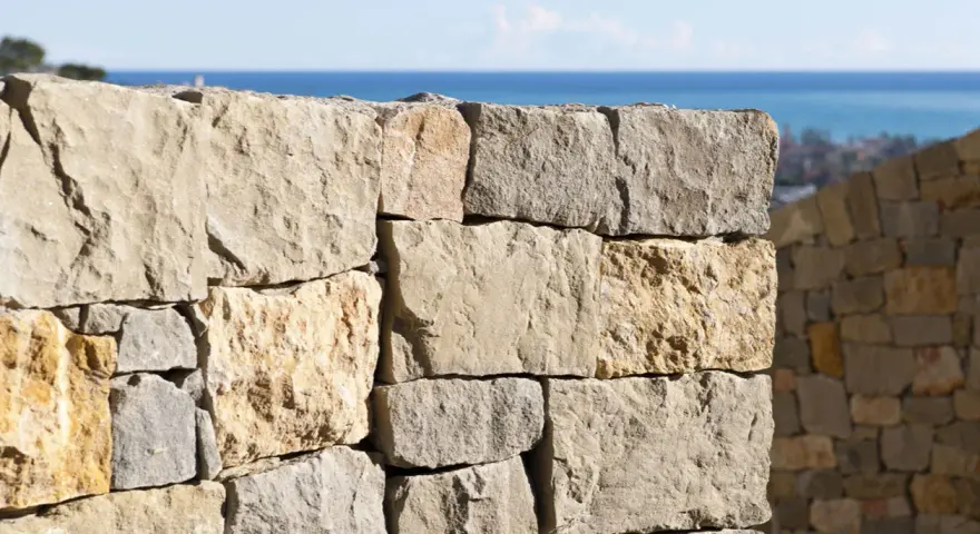 Muro a secco per contenimento terra, con vista sul mare e un borgo in lontananza.