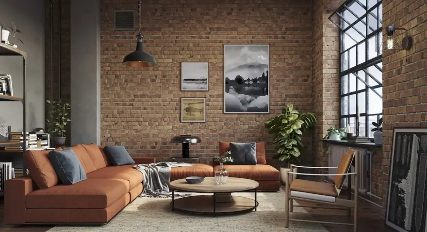Soggiorno con divano arancione, tavolino rotondo e poltrona in legno. Pareti in mattoni a vista e grande finestra definiscono l'arredamento industrial chic.