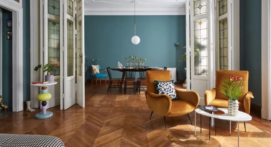 Salotto con poltrone ocra, tavolino dal design moderno e porte a soffietto con vetri decorati, un mix di stile vintage e contemporaneo.