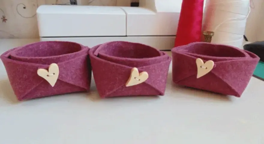 Tre cestini in feltro fai da te, color melanzana, decorati con bottoni a forma di cuore. Perfetti per organizzare piccoli oggetti.
