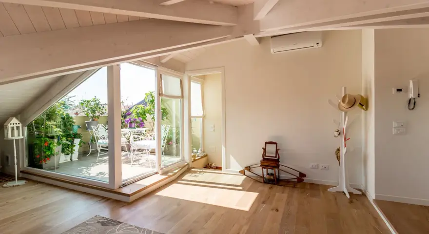 Luminoso sottotetto con travi a vista e un terrazzo fiorito. Idee sottotetto molto basso per sfruttare ogni angolo.