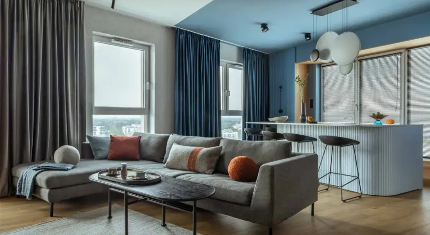 Soggiorno moderno con divano grigio, tavolino nero e tende blu e grigie. Un esempio di come scegliere le tende per il salotto per un look sofisticato.