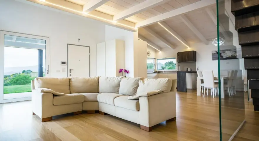 Soggiorno moderno con travi in legno sbiancate senza carteggiare, divano beige e cucina a vista.