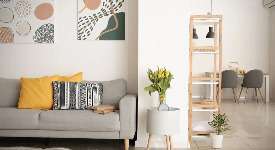 Soggiorno moderno con divano grigio, cuscini gialli e decorazioni astratte. Si nota la differenza tra ammobiliato e arredato: qui, ogni elemento è scelto con cura per creare un ambiente accogliente.