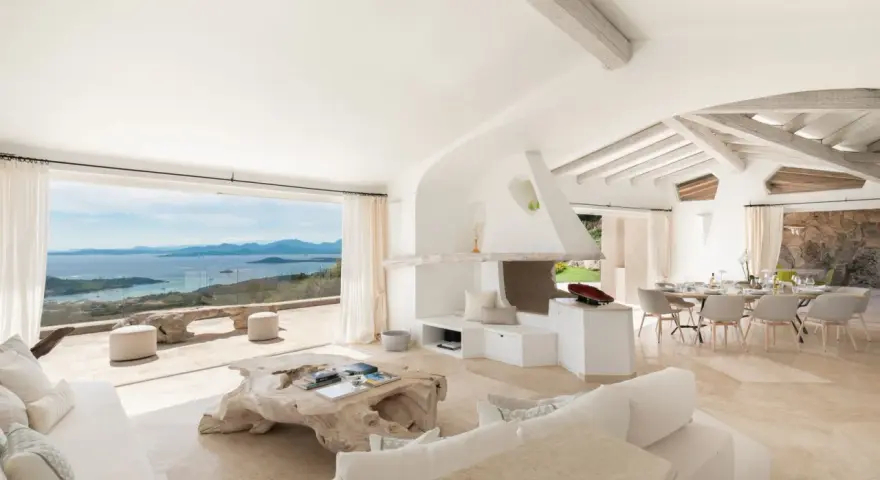 Soggiorno luminoso con vista mare, perfetto per l'arredo case al mare. Divani bianchi, camino moderno e tavolo da pranzo per godersi il panorama.