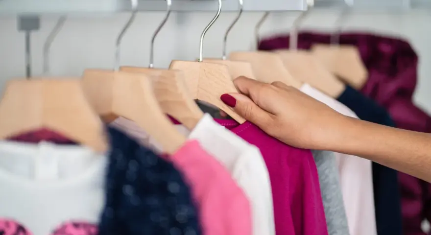 Mano che sistema vestiti colorati su grucce di legno, un'idea per come organizzare armadio bambini.