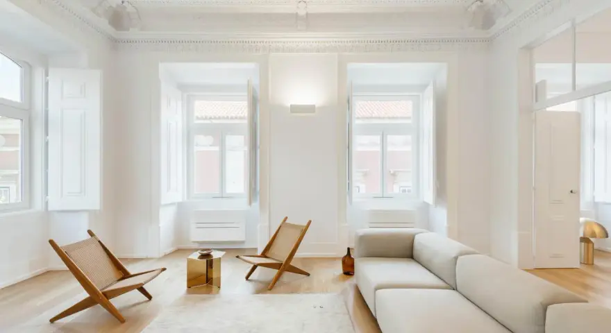 Soggiorno minimalista con divano chiaro, sedie in legno e tavolino dorato. Un esempio di come un consulente d'arredo può creare un ambiente luminoso e accogliente.