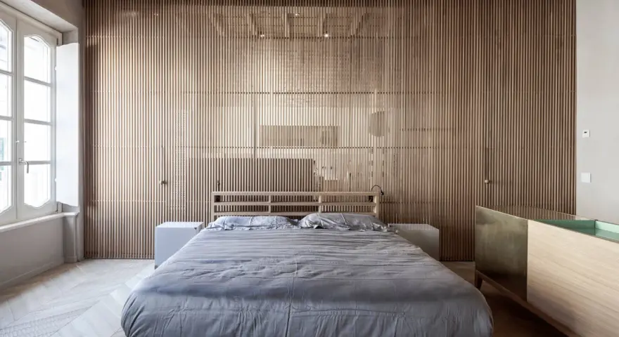 Camerette con separè in legno che creano un ambiente caldo e moderno. Letto matrimoniale con biancheria grigia e comodini bianchi.
