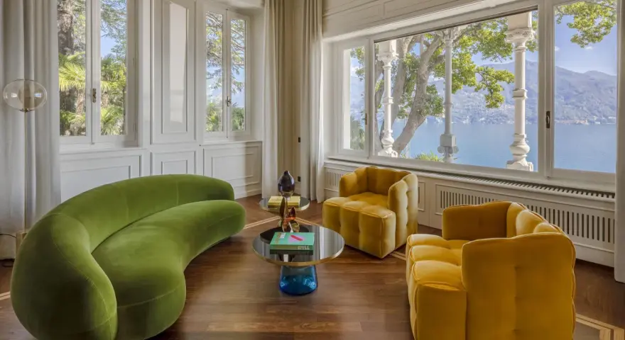 Un salotto con divano verde curvo e poltrone gialle, tavolini rotondi e vista lago. Un perfetto esempio di **art deco arredamento** con tocchi moderni.