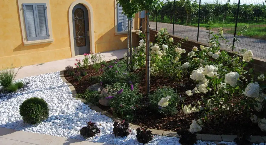 Giardini idee da copiare: un angolo con ghiaia bianca, arbusti verdi e ortensie bianche.