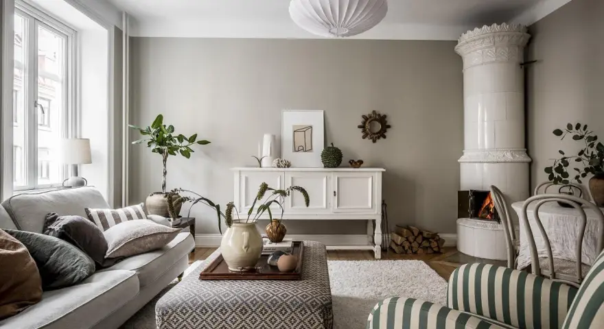 Salotto accogliente con camino in maiolica, divano grigio e pouf decorato. L'arredamento stile classico si fonde con elementi moderni.