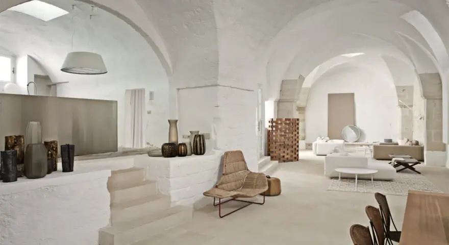 Interni moderni con soffitti a volta, un'elegante cucina a vista, zona living con divani e poltrone in vimini, e dettagli decorativi in ceramica.