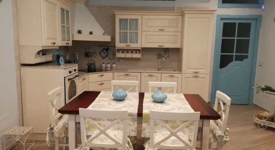 Accogliente piccola tavernetta casa con cucina in legno chiaro, tavolo da pranzo e porta azzurra.