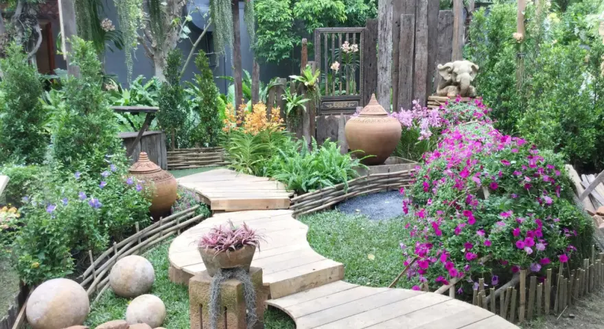 Percorso sinuoso in legno tra fiori vivaci e vasi in terracotta, con elementi decorativi che evocano idee giardino zen.