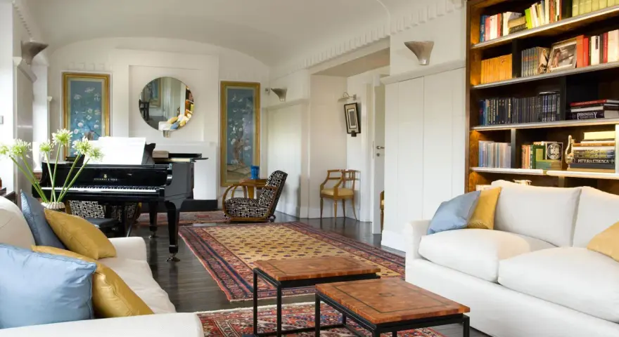 Salotto con pianoforte a coda, divani bianchi, tappeti orientali e libreria. Un perfetto esempio di arredamento classico moderno.