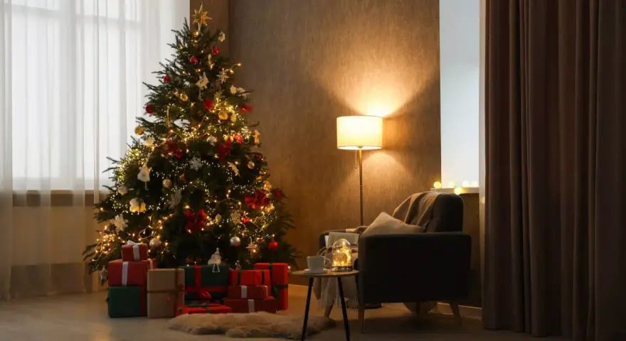Un accogliente soggiorno con un **albero di Natale stile scandinavo** illuminato, circondato da regali. Una poltrona invitante e una lampada creano un'atmosfera calda.