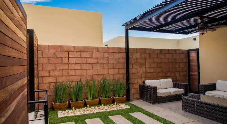 Un cortile in cemento trasformato con erba sintetica, piante in vaso e arredi da esterno. Idee per come abbellire un cortile in cemento.