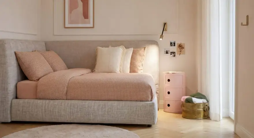 Un angolo letto con biancheria a quadri, cuscini morbidi e un quadro astratto. L'ambiente è accogliente, perfetto per creare camere aesthetic.