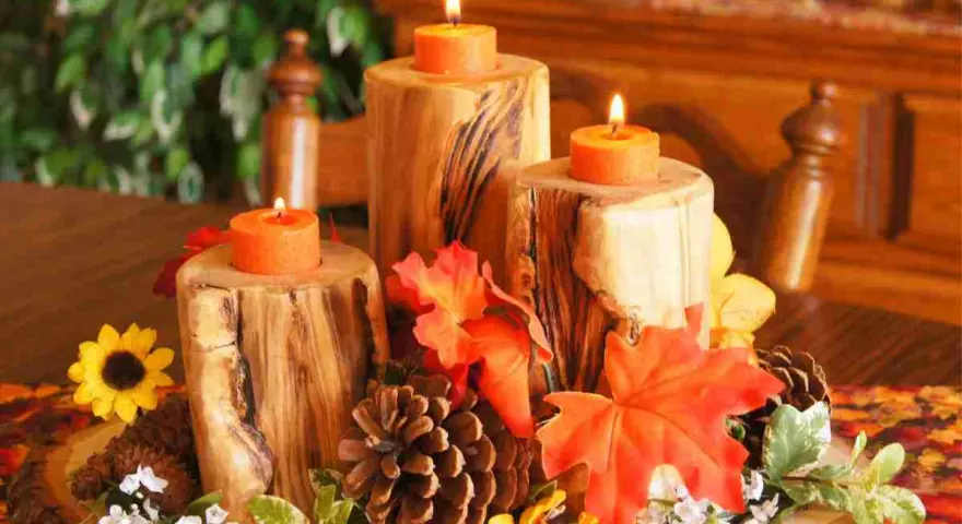 Un semplice centrotavola autunnale con tronchi di legno, candele arancioni, pigne e foglie colorate.
