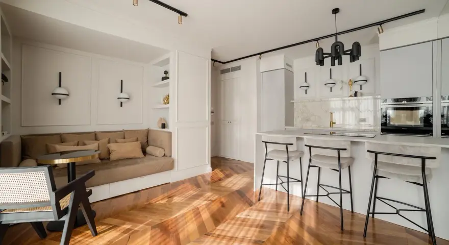 Open space con ingresso aperto su soggiorno. Divano angolare, bancone cucina con sgabelli e parquet a spina di pesce.