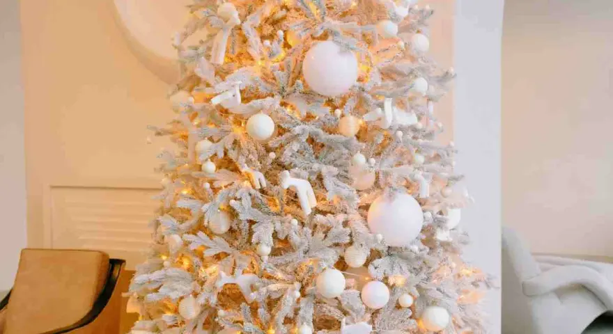 Albero di Natale innevato con luci calde, palline bianche e dorate, e decorazioni a forma di angeli e cervi. Un'elegante idea per un albero di Natale bianco e oro.