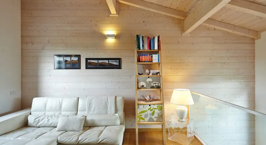 Soggiorno accogliente con divano bianco, libreria a giorno e un suggestivo tetto in legno a vista.