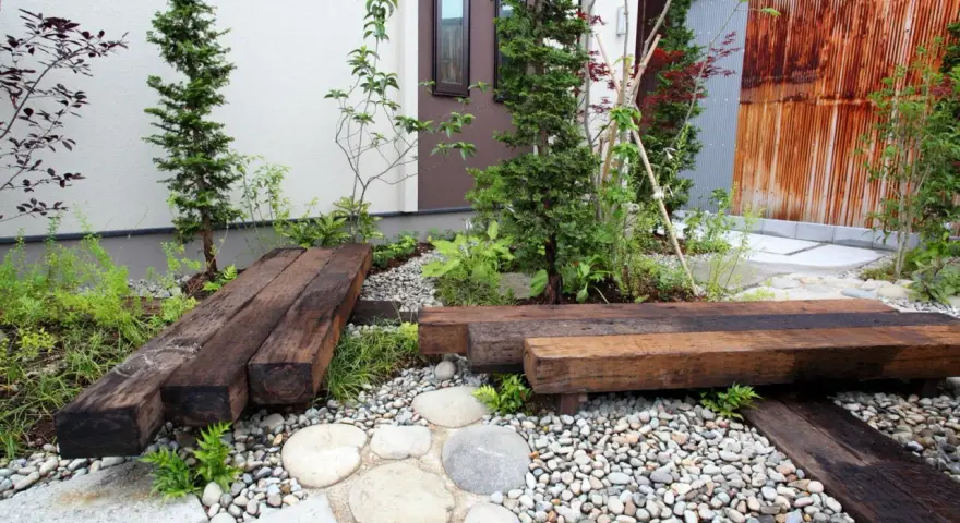Un piccolo giardino zen con panchine in legno riciclato, ghiaia e piante verdi. Perfetto per idee giardino piccolo fai da te.