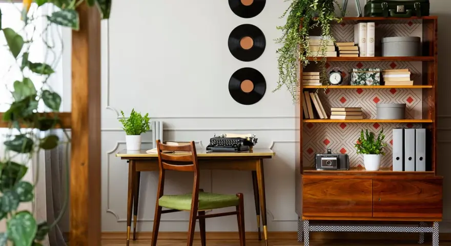 Scrivania con macchina da scrivere e sedia verde, libreria con dischi in vinile e piante. Perfette idee arredamento vintage per un angolo studio.