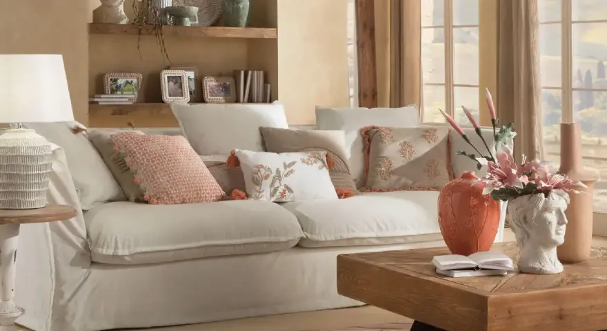 Divano bianco con cuscini decorati, lampada e tavolino in legno creano un'atmosfera di **stile cozy**.