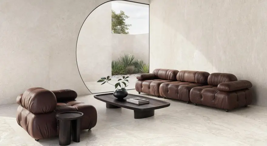 Salotto moderno con divano e poltrona in pelle marrone, tavolino in legno scuro e vista su un giardino interno. L'ambiente evoca la serenità di una casa provenzale.
