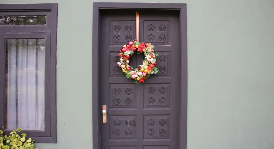 Ghirlanda natalizia appesa con un nastro alla porta scura, un esempio di come appendere la ghirlanda alla porta per le feste.