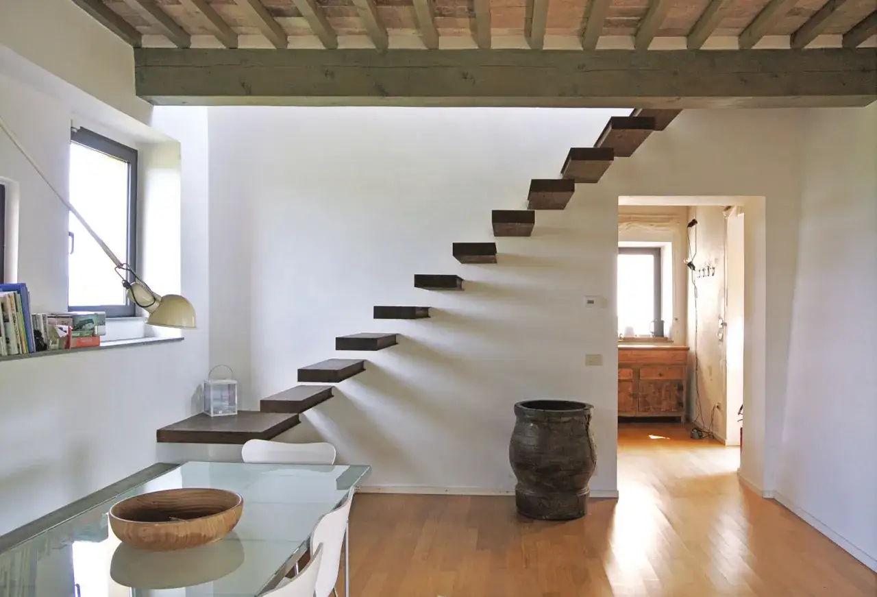 Scale sospese in una casa moderna, con un tavolo di vetro e una grande anfora. Un esempio di case bellissime.