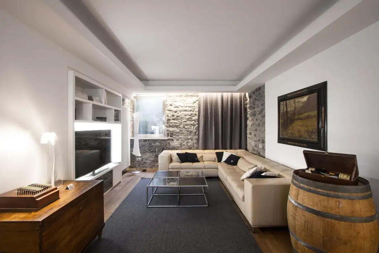 Salotto con divano angolare beige, tavolino in vetro, mobile TV, un quadro e una botte di vino. Stile contemporaneo chic.