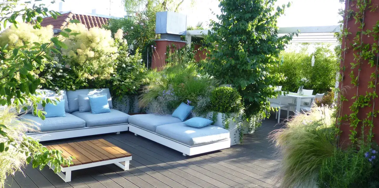 Un lussureggiante giardino sul terrazzo fai da te con divani comodi, tavolino e un tavolo da pranzo, circondato da piante rigogliose.