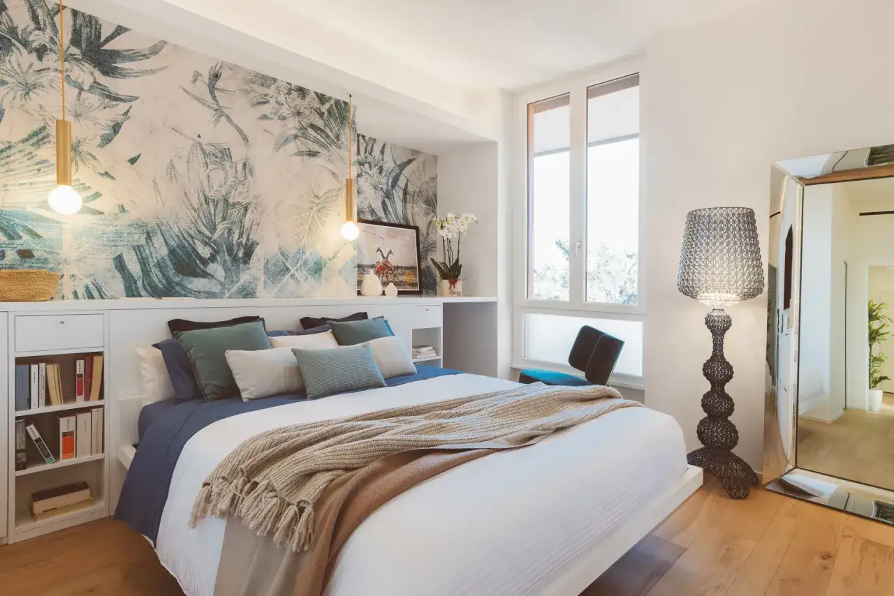 Accogliente camera da letto stile mediterraneo con carta da parati floreale, letto comodo e grande specchio.