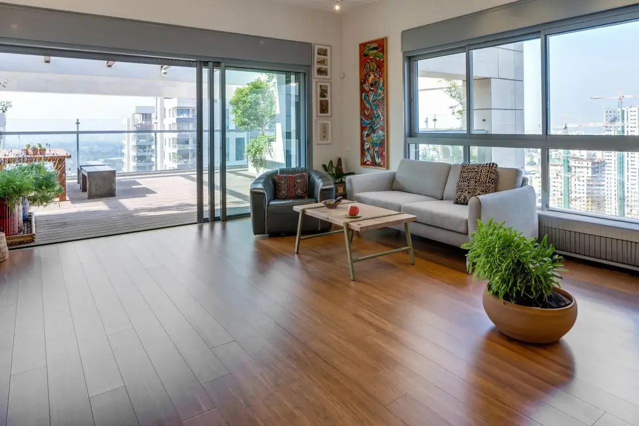 Soggiorno con divano grigio, poltrona in pelle, tavolino in legno e un quadro colorato. Ampie vetrate offrono una vista sulla città, incarnando perfetti stili di arredamento contemporaneo.