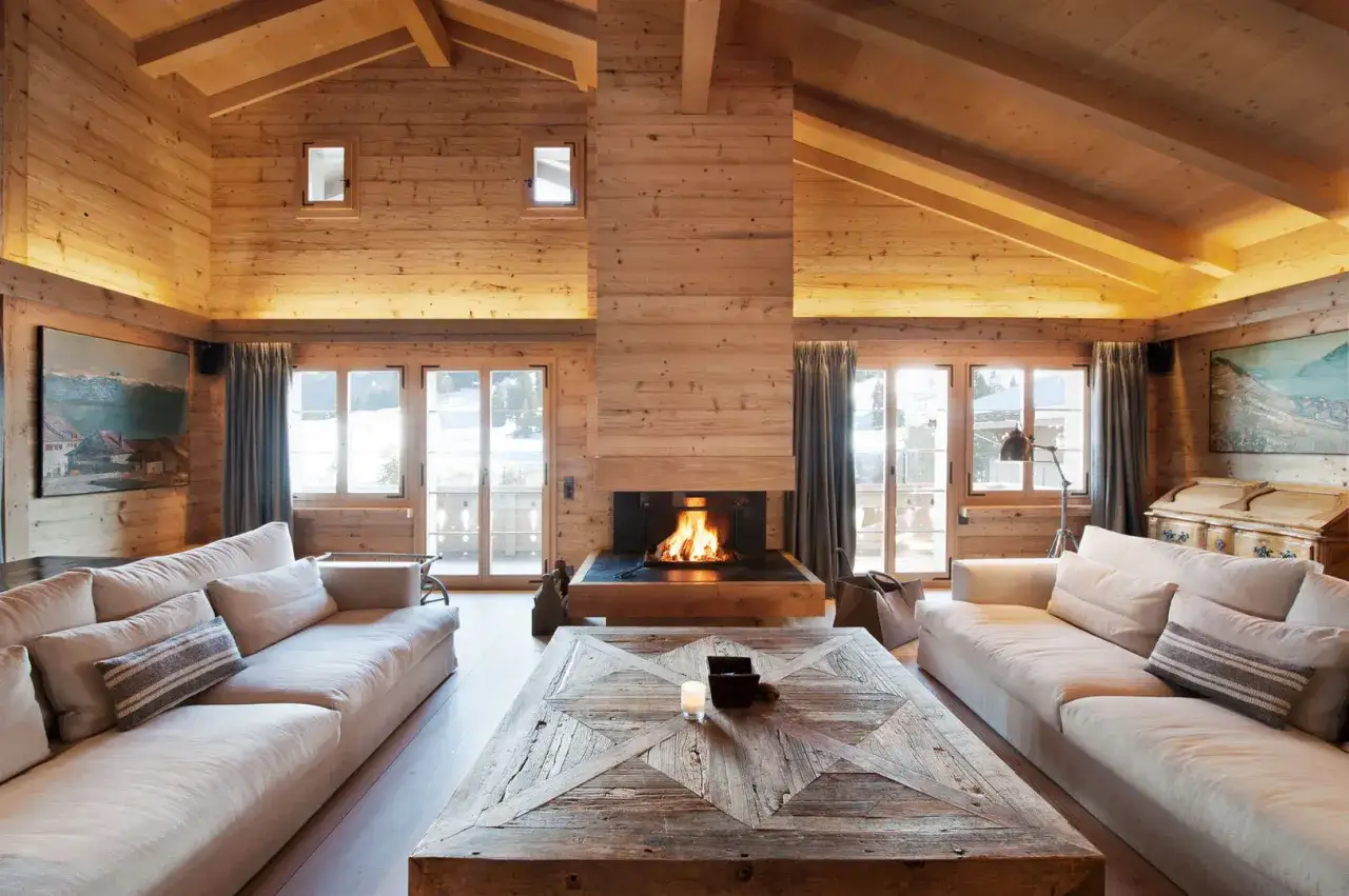 Accogliente soggiorno in legno con camino acceso, divani chiari e un grande tavolino rustico. L'arredamento stile contemporaneo si fonde con elementi naturali.