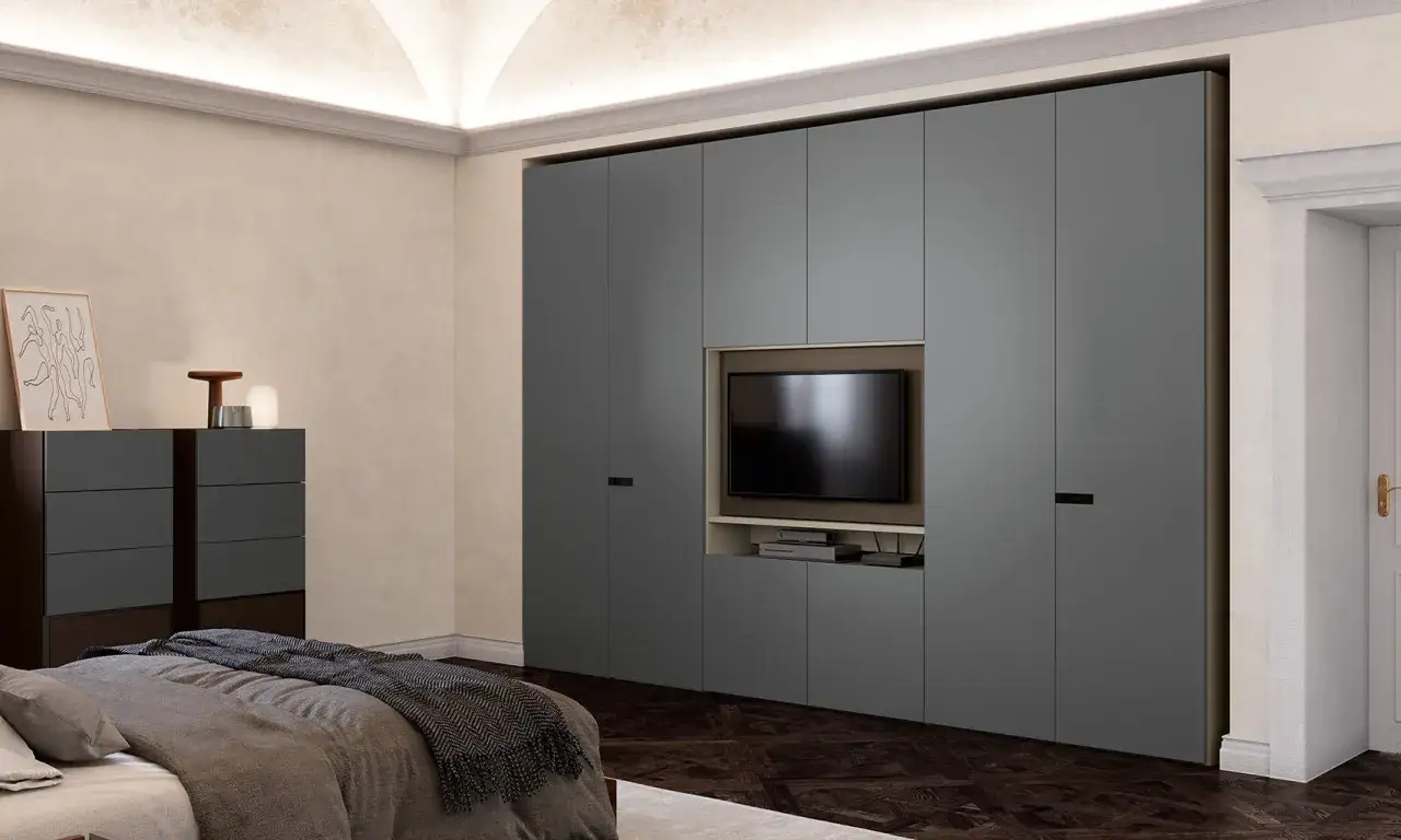 Armadio grigio con nicchia centrale per la posizione TV camera da letto. Sotto, mensole e vani contenitori.
