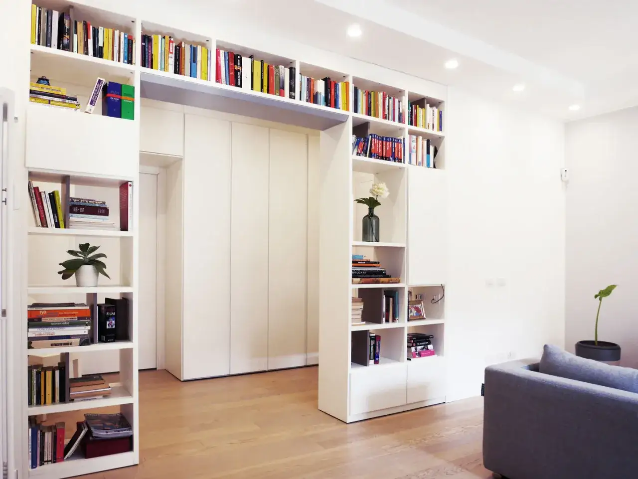 Ampia libreria a ponte bianca, piena di libri e oggetti decorativi, domina la stanza.