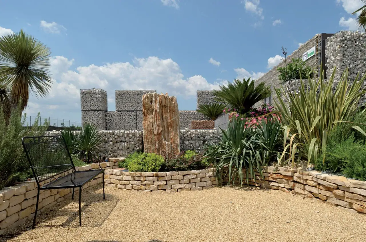 Giardino moderno con palme, seduta in ferro e muretti in pietra. Idee giardino con palme per un'oasi di relax.