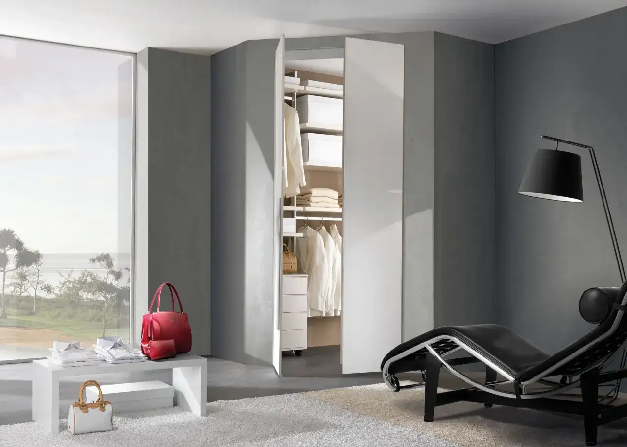 Idee cabina armadio piccola: un angolo elegante con abiti ordinati, borse rosse e bianche, e una chaise longue nera.