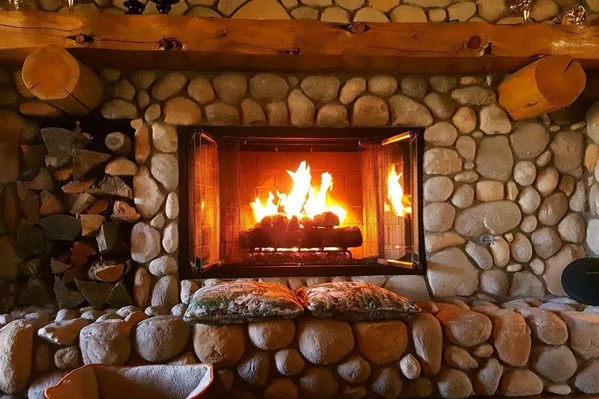 Camino in pietra e legno, con fuoco acceso. Perfetto per idee camini rustici di montagna, evoca calore e accoglienza.