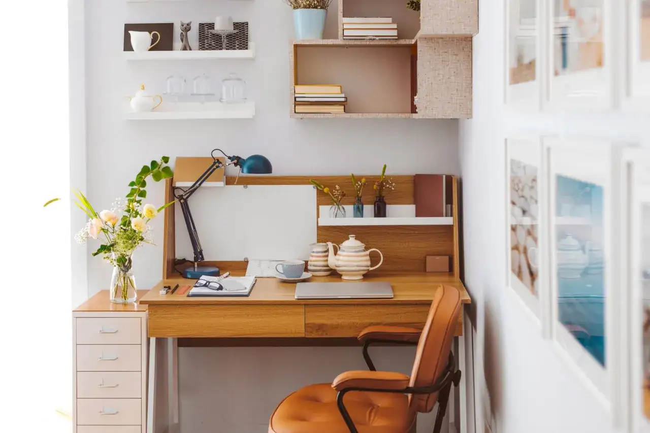 Scrivania in legno con lampada, fiori, tazza, teiera e laptop. Ottime idee organizzazione scrivania per uno spazio di lavoro funzionale e accogliente.