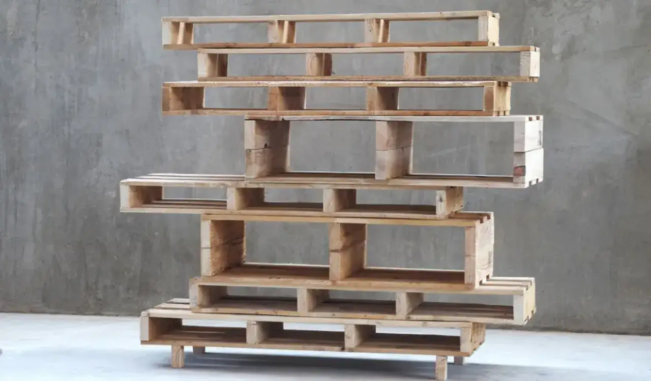 Libreria fai da te con pallet in legno grezzo, impilati in modo asimmetrico per creare vani contenitori.