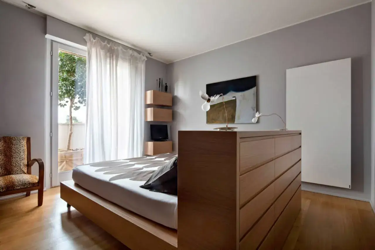 Un moderno letto in mezzo alla stanza, con un copriletto a motivi floreali, accanto a una poltrona leopardata e una cassettiera in legno.