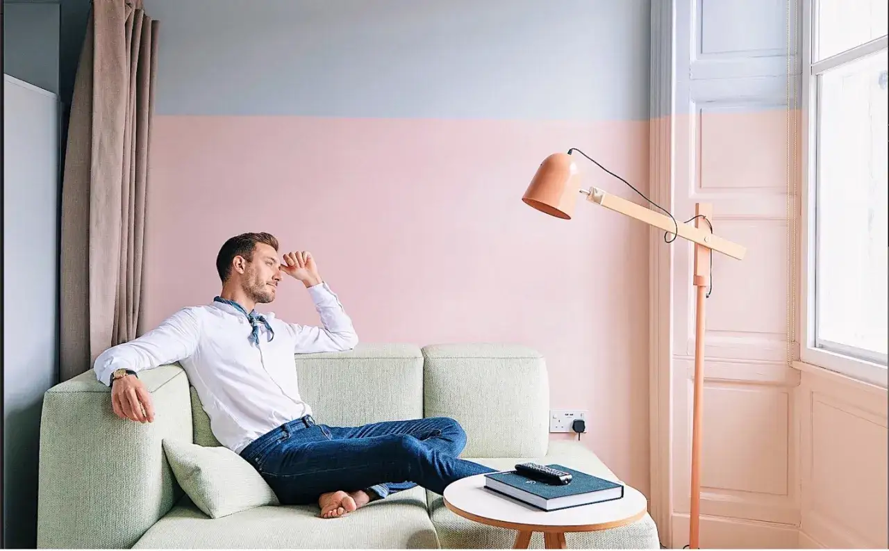 Uomo su divano in un ambiente con pareti bicolore rosa e grigio. Idee per come rivestire una parete interna in modo economico.