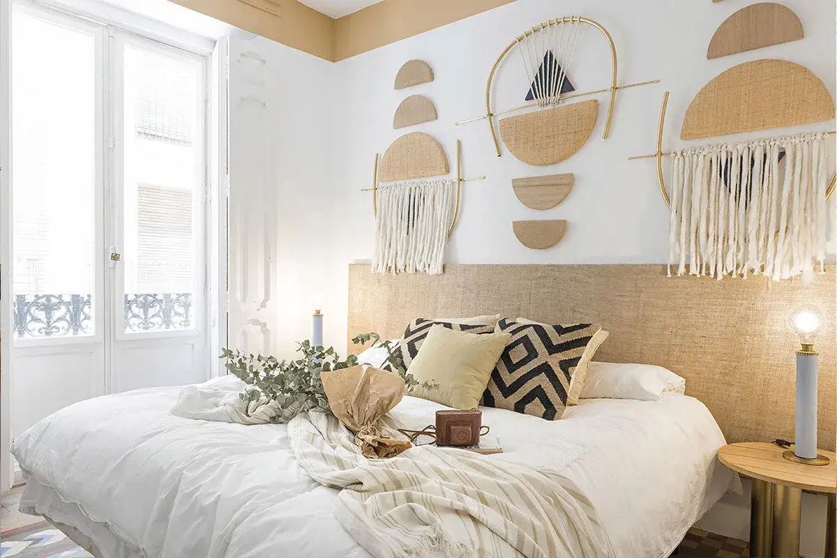 Accogliente camera da letto stile boho con decorazioni murali in paglia e macramè, letto bianco e dettagli in legno.