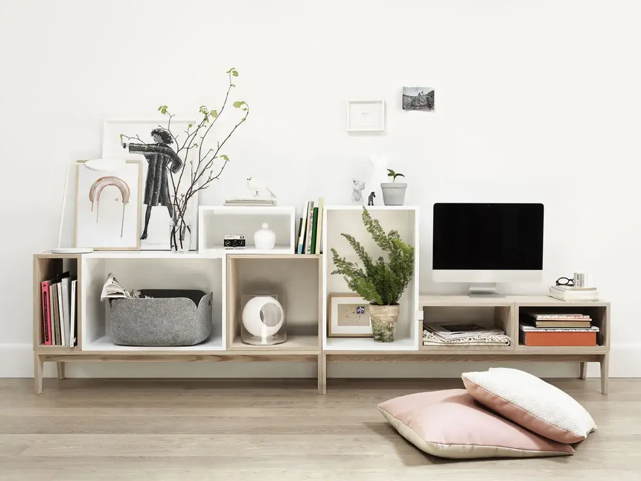 Arredare casa con pochi soldi: mobile basso con vani a giorno, cestino grigio, piante, quadri e computer.